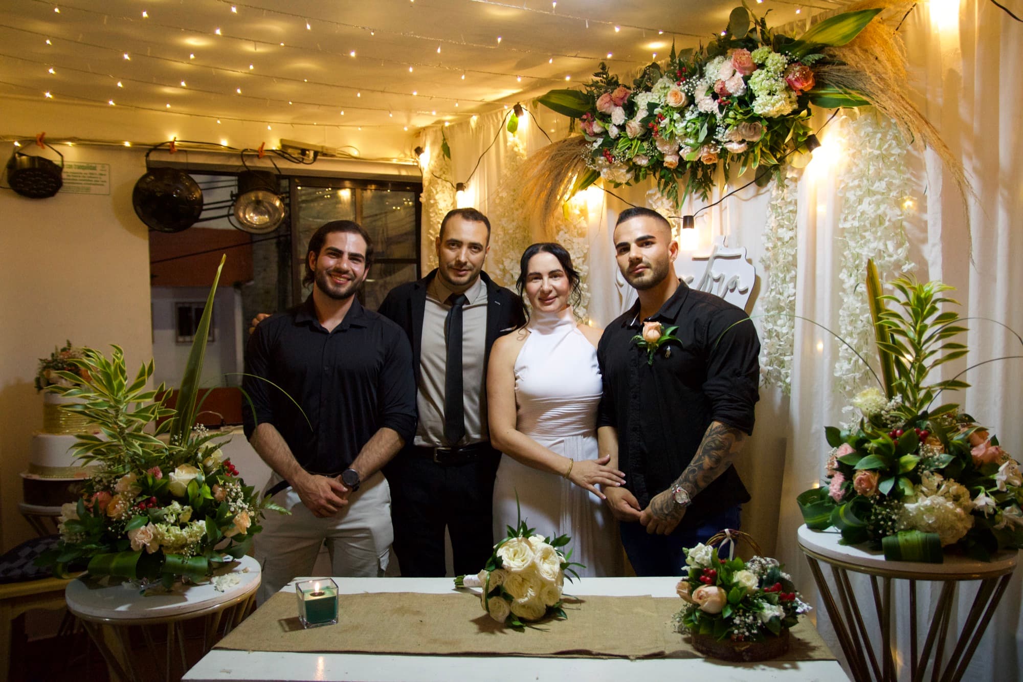 Los novios posando con dos invitados delante del arco de flores